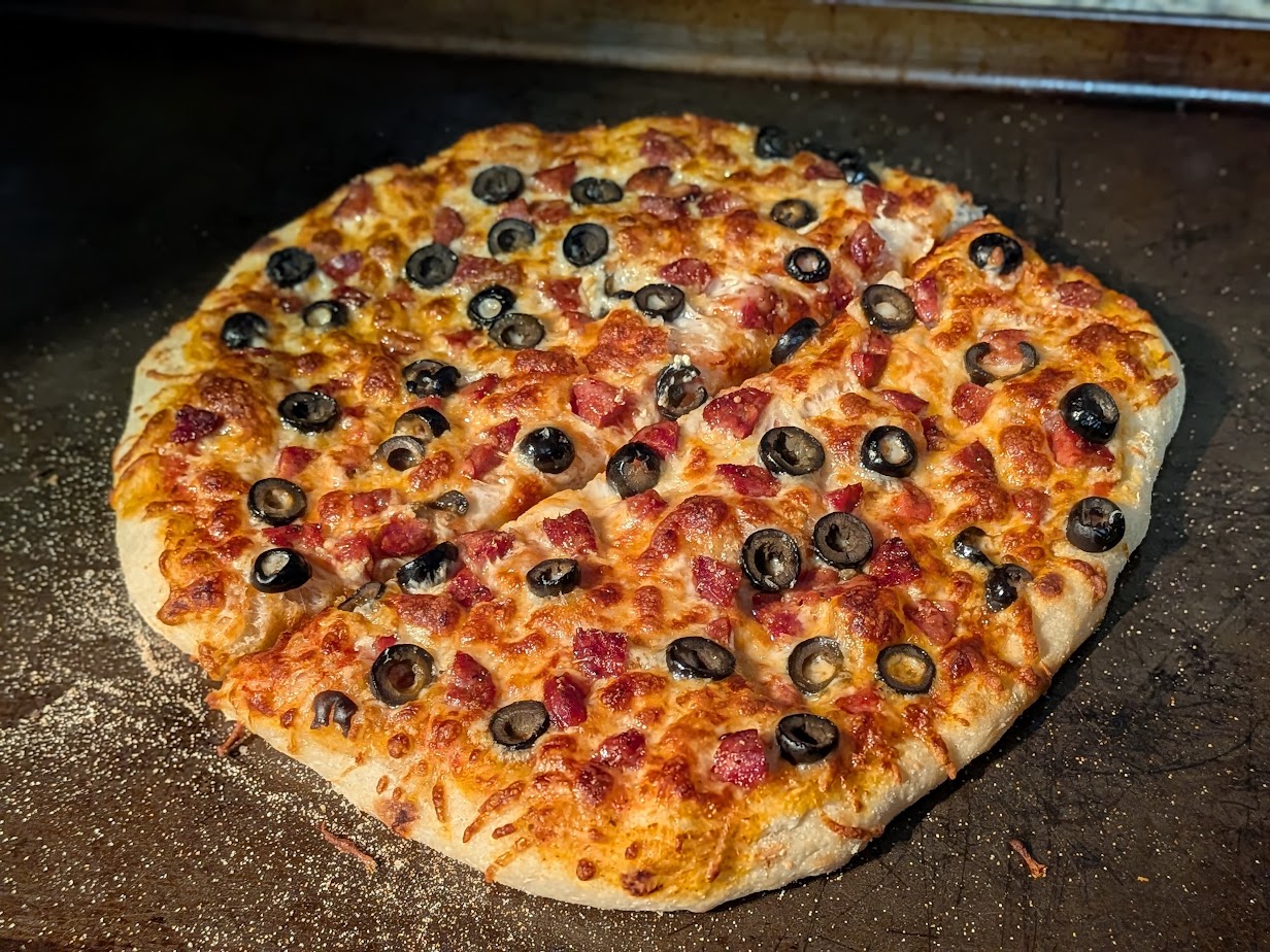 Sourdough New York style pizza topped with diced andouille sausage, sliced black olives, and melted mozzarella, baked on a pizza stone