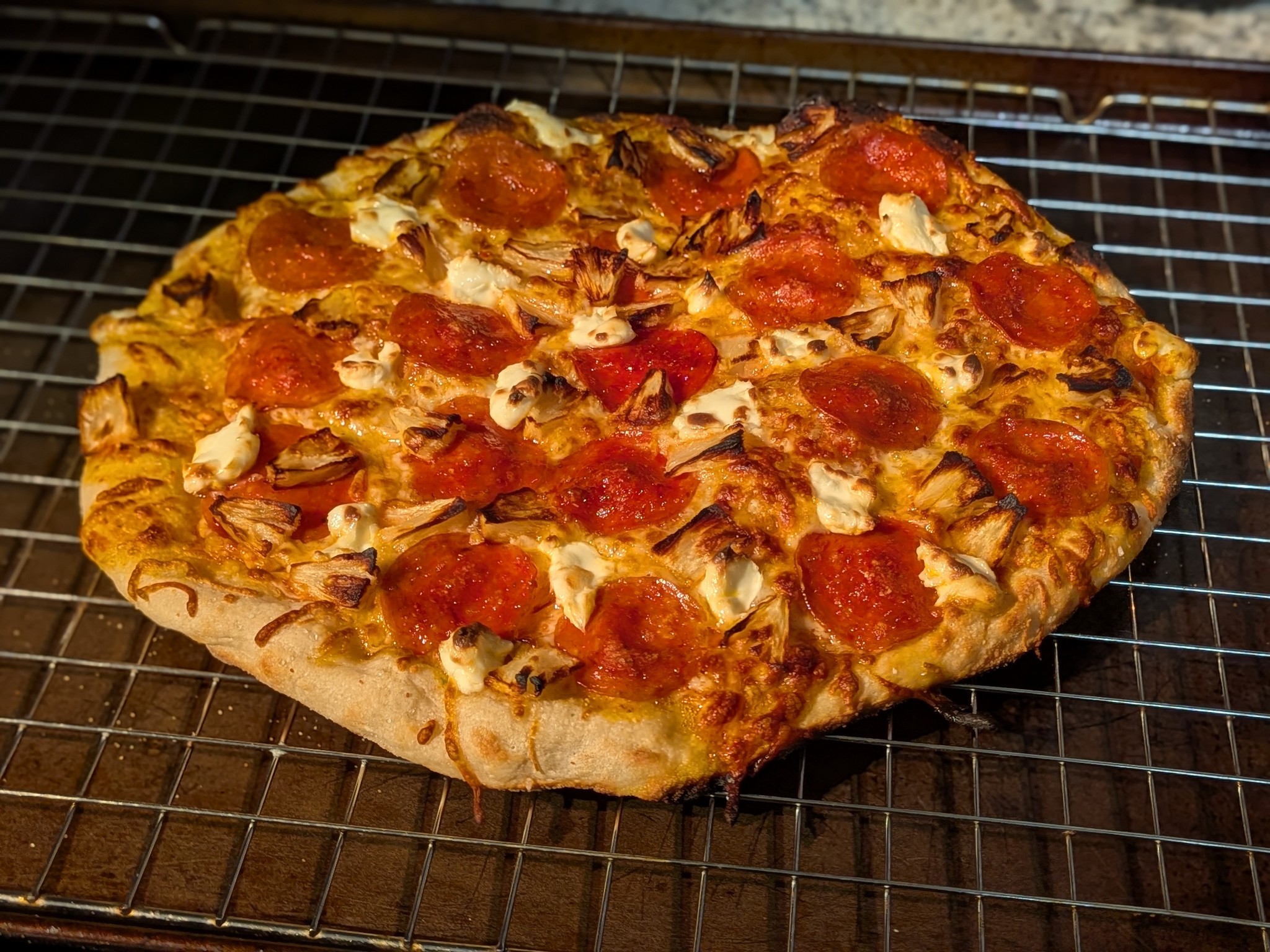 Sourdough New York style pizza topped with pepperoni, roasted pineapple wedges, and dollops of cream cheese, cooling on a wire rack
