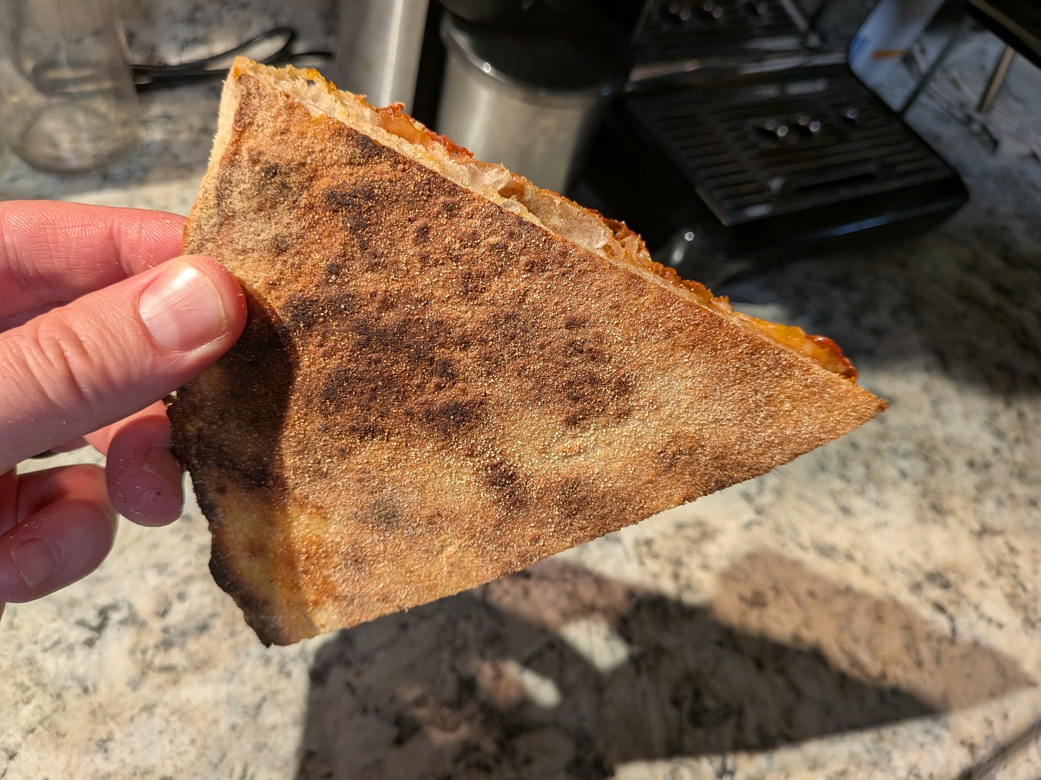 Underside of a sourdough New York pizza slice showing leoparding and char from a 550°F home oven bake on a pizza stone