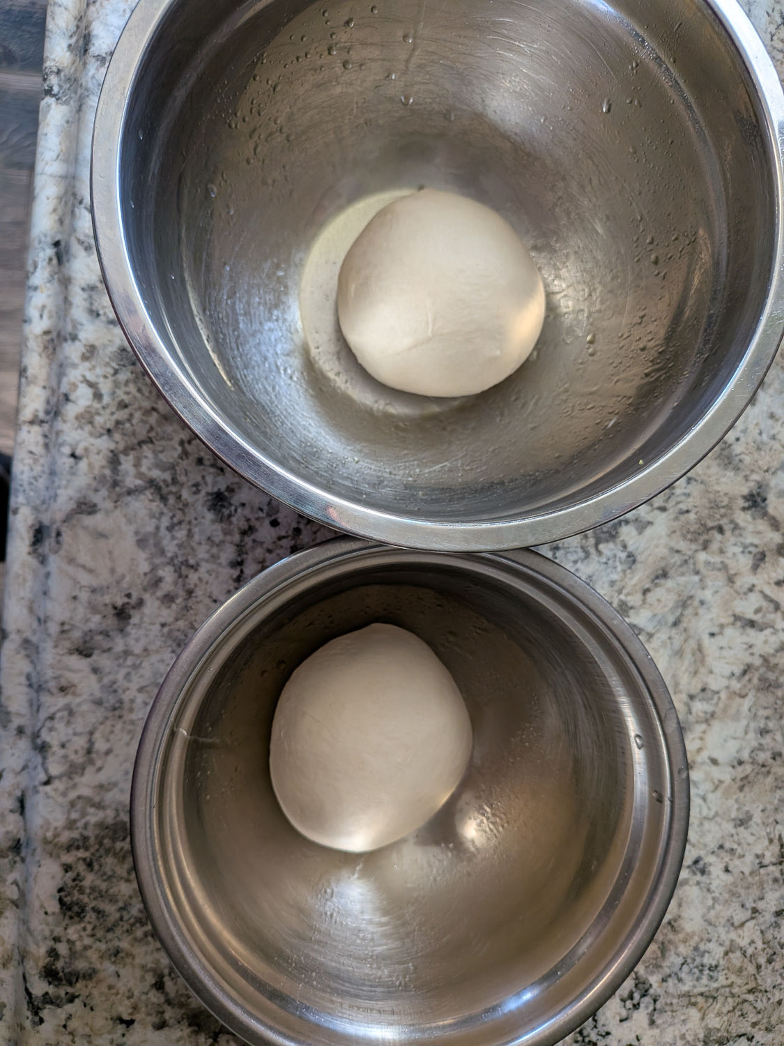 Two same-day sourdough dough balls resting in stainless steel bowls after the bulk ferment, before stretching for tavern-style pizza