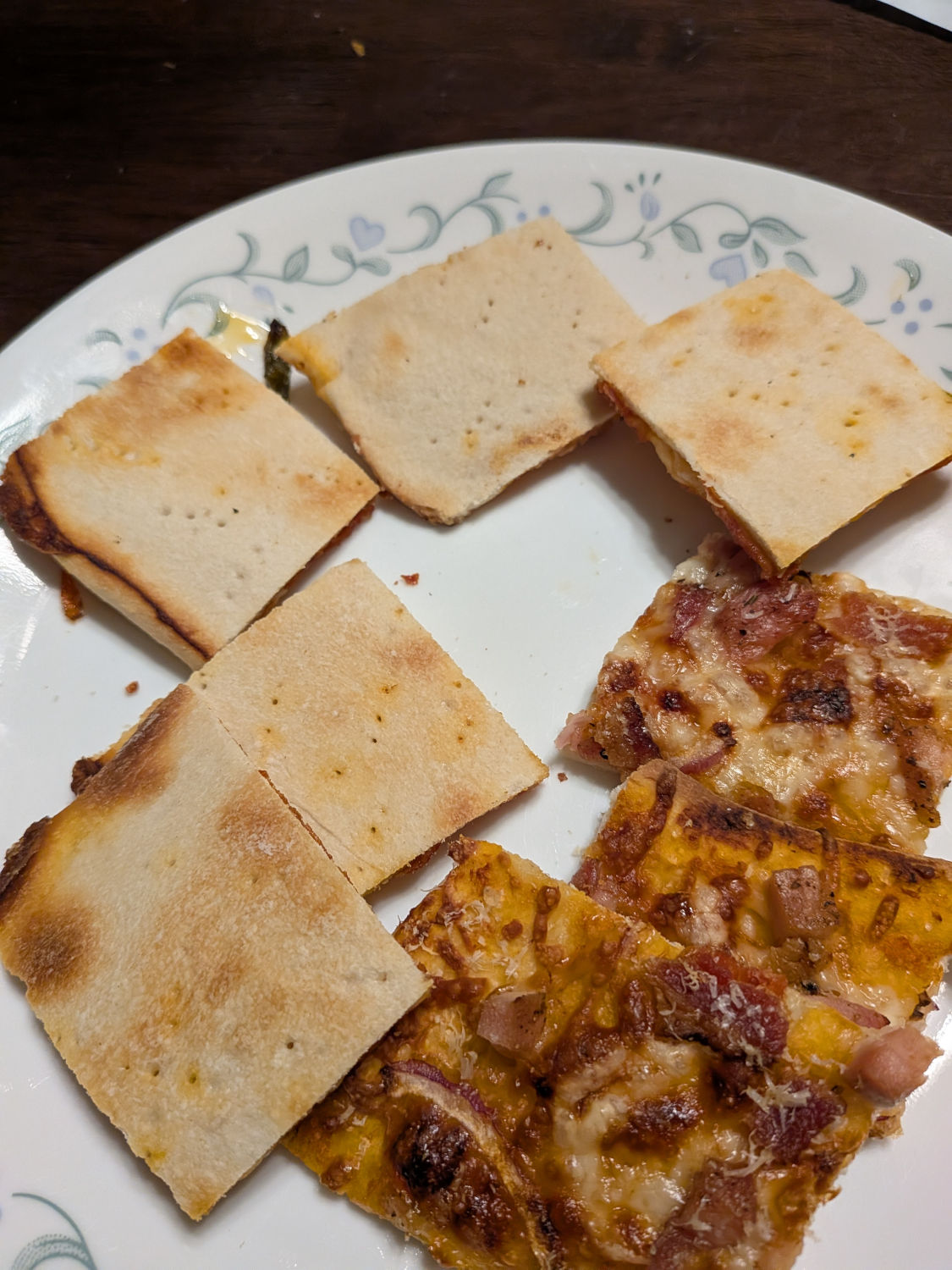 Several tavern-style pizza squares on a decorative plate showing the cracker-thin crust alongside a saucy slice with bacon and red onion