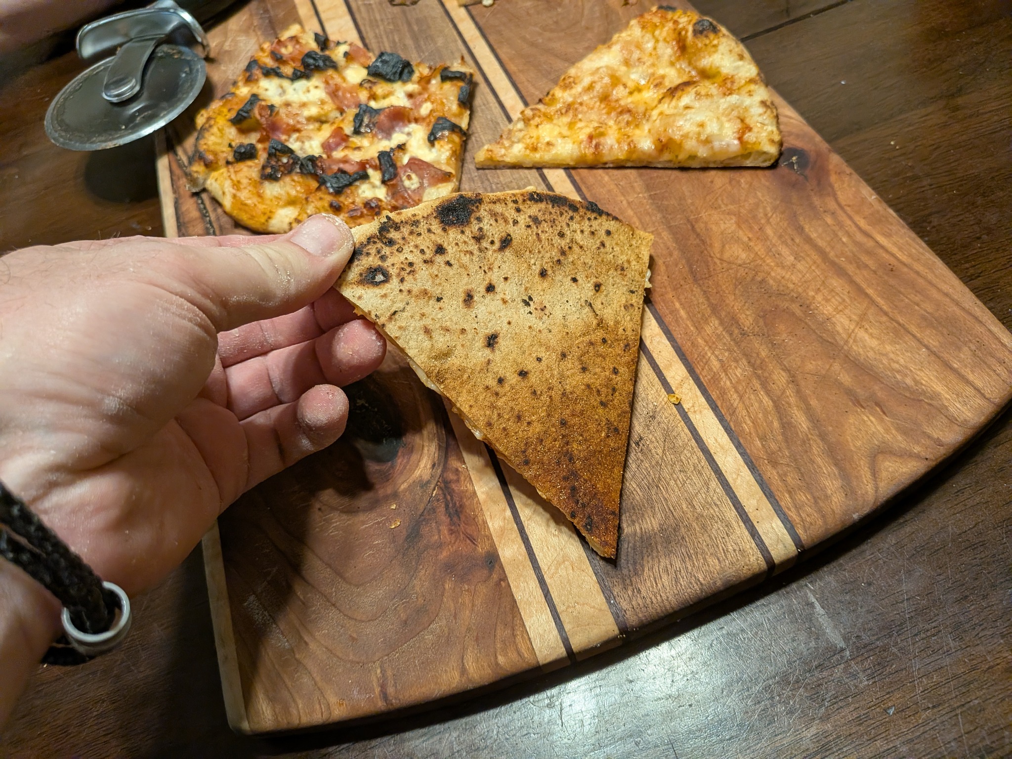 Hand holding a sourdough Neapolitan pizza slice from the Ooni Koda 16 with a noticeably burnt, charred bottom
