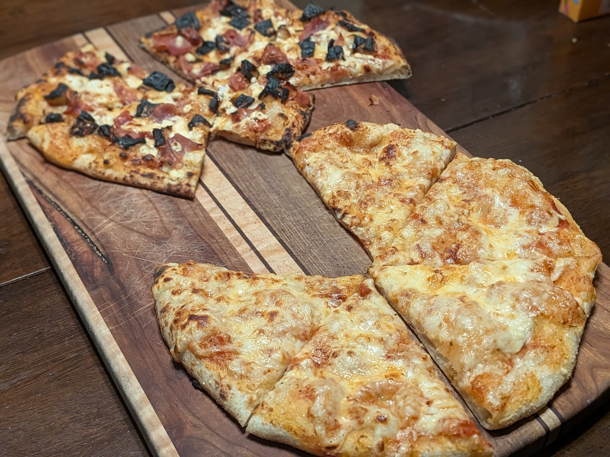 Two cooked sourdough Neapolitan pizzas on a wood cutting board, plain cheese in the foreground and Italian sausage with black olives in back, baked on the Ooni Koda 16