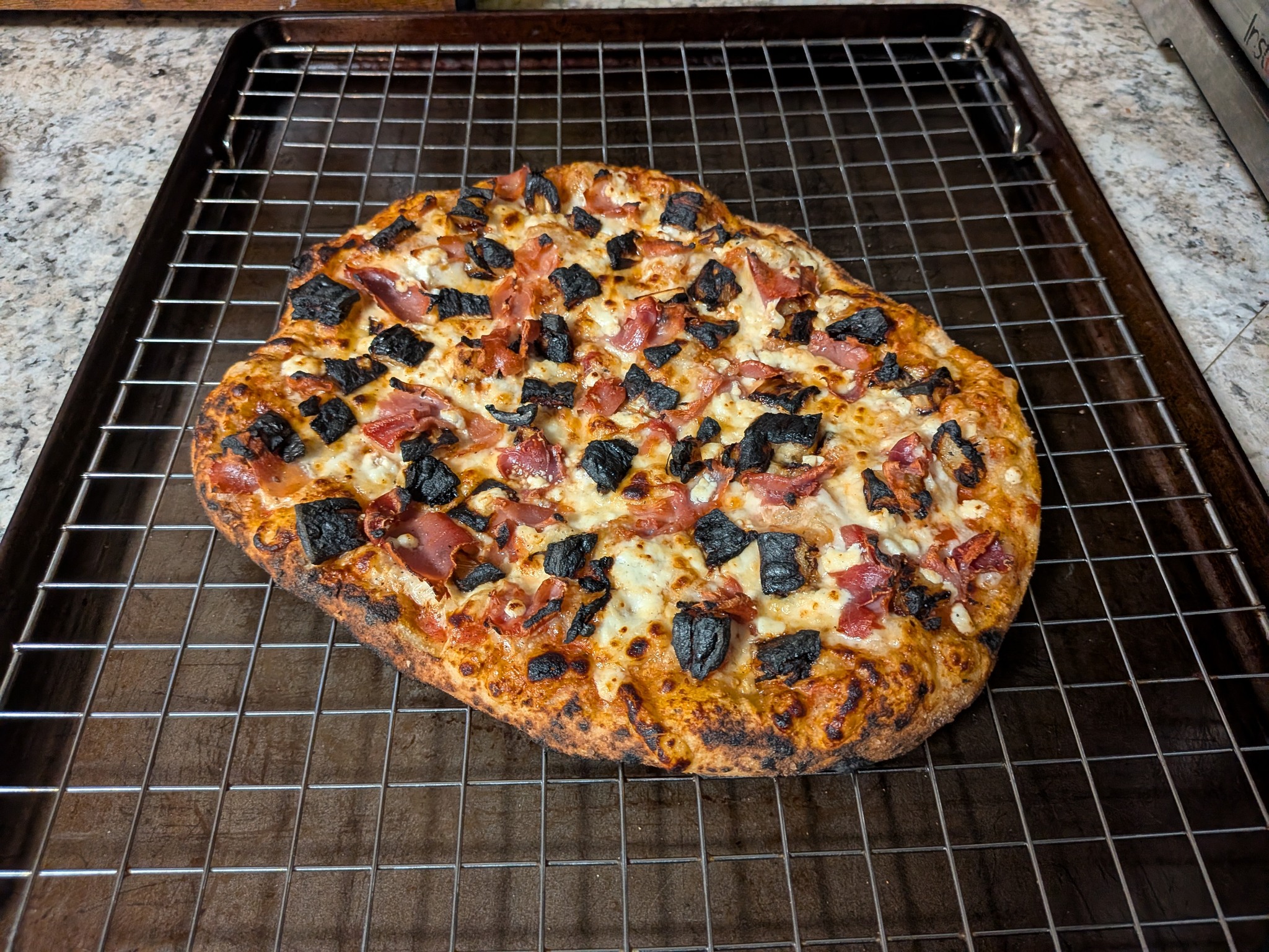 Baked Fancy Hawaiian sourdough Neapolitan pizza on a cooling rack with prosciutto, charred roasted pineapple, and crumbled goat cheese