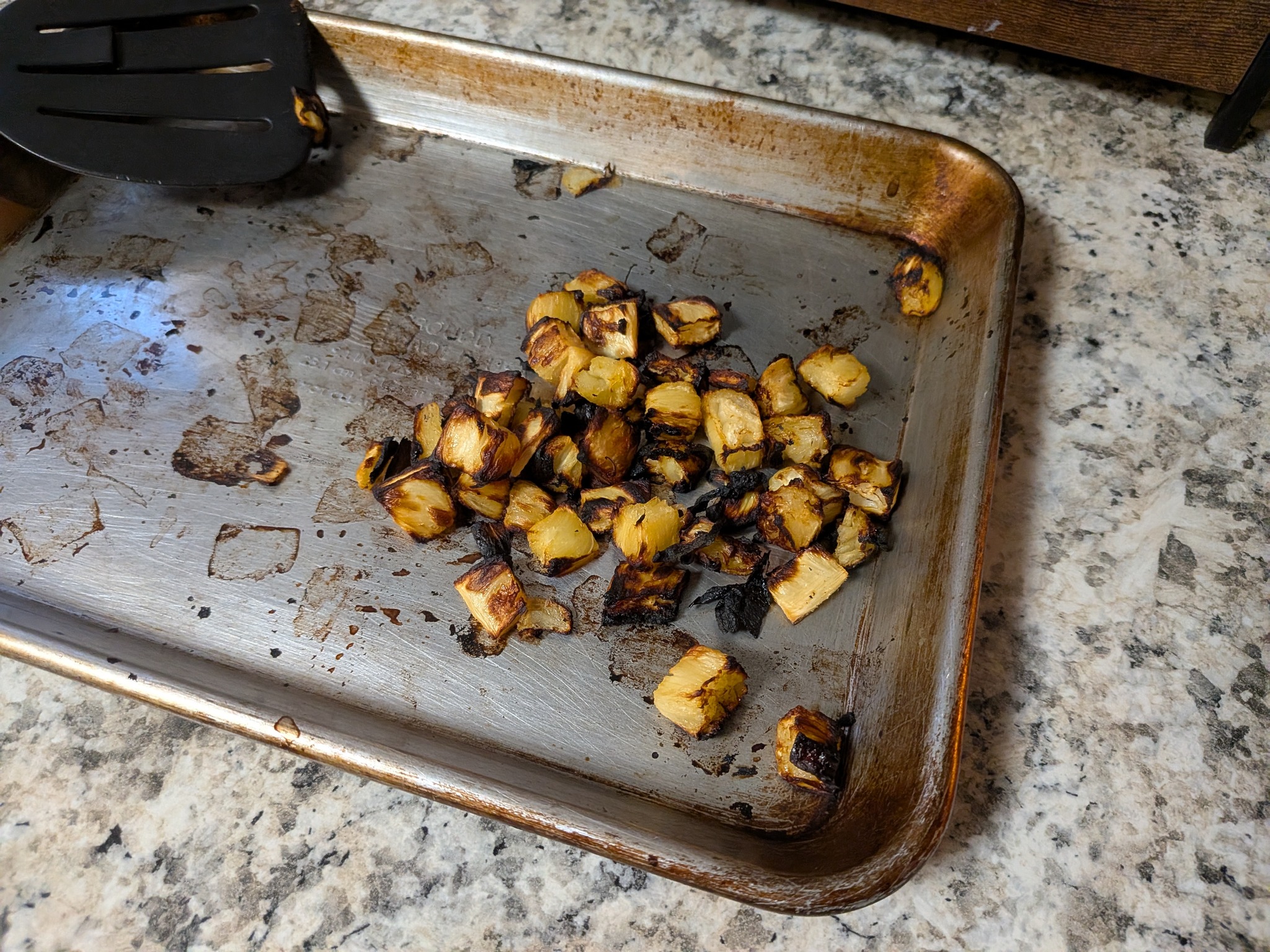 Heavily over-roasted, charred pineapple cubes on a sheet pan after losing track of them in the oven, before topping the Fancy Hawaiian pizza