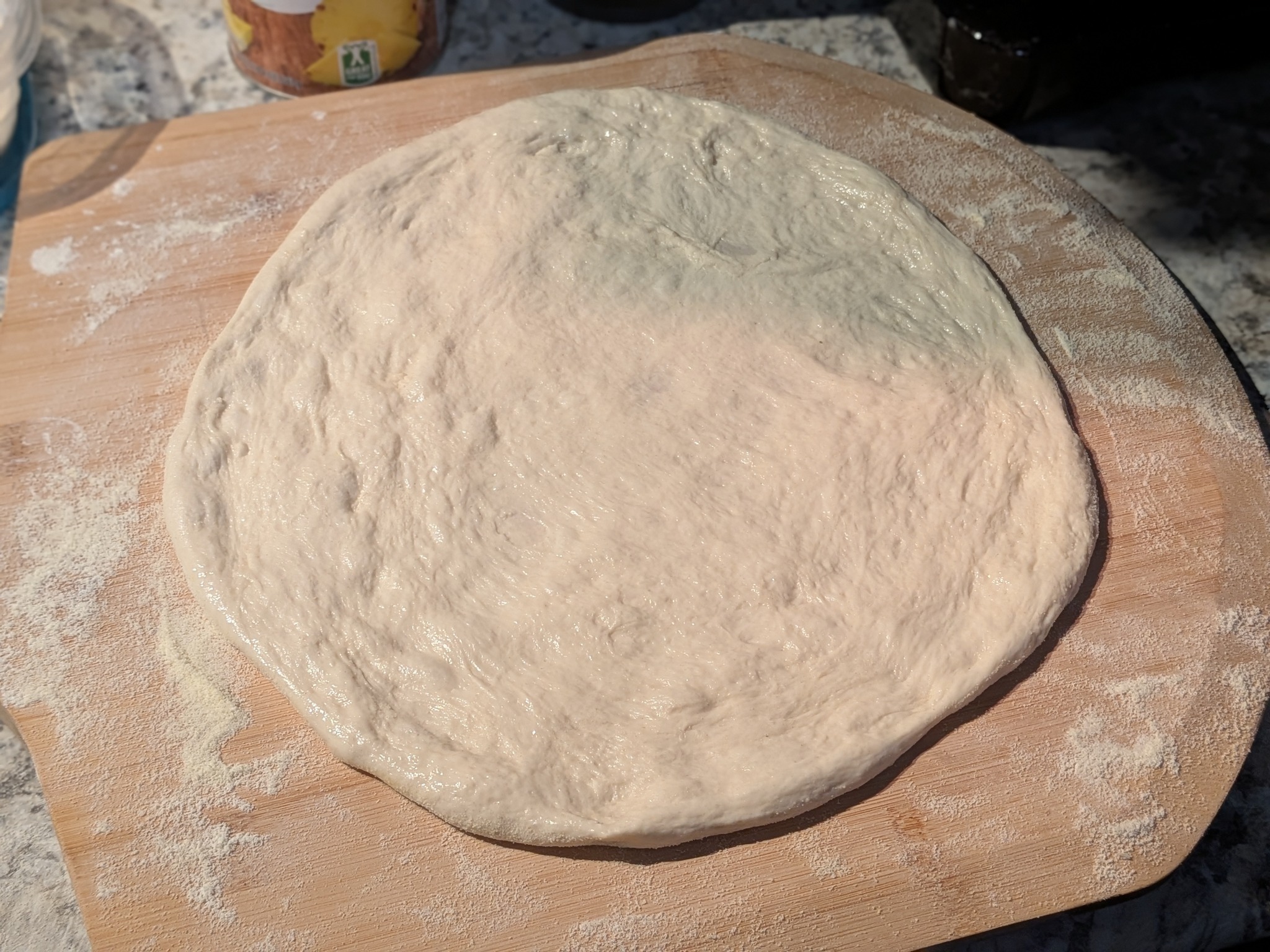 Hand-stretched cold-fermented sourdough Neapolitan dough disc on a floured wooden peel, before topping