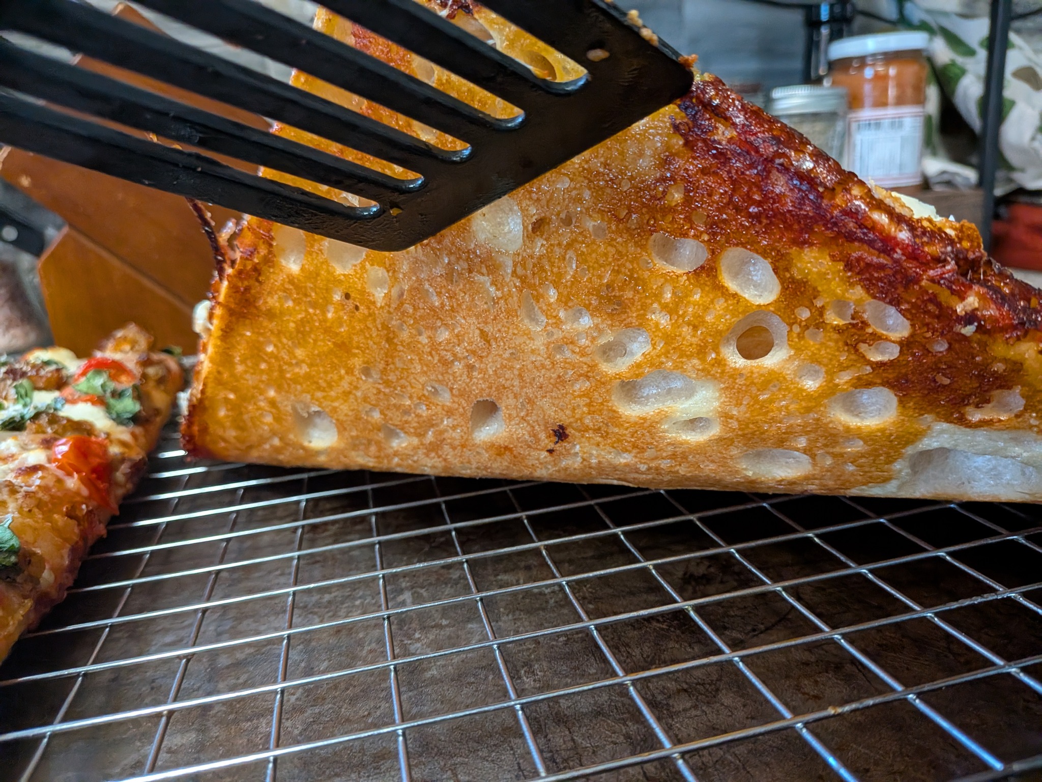 Spatula lifting a Sicilian grandma pan pizza slice showing the deeply caramelized frico cheese edge and the airy, open crumb structure inside
