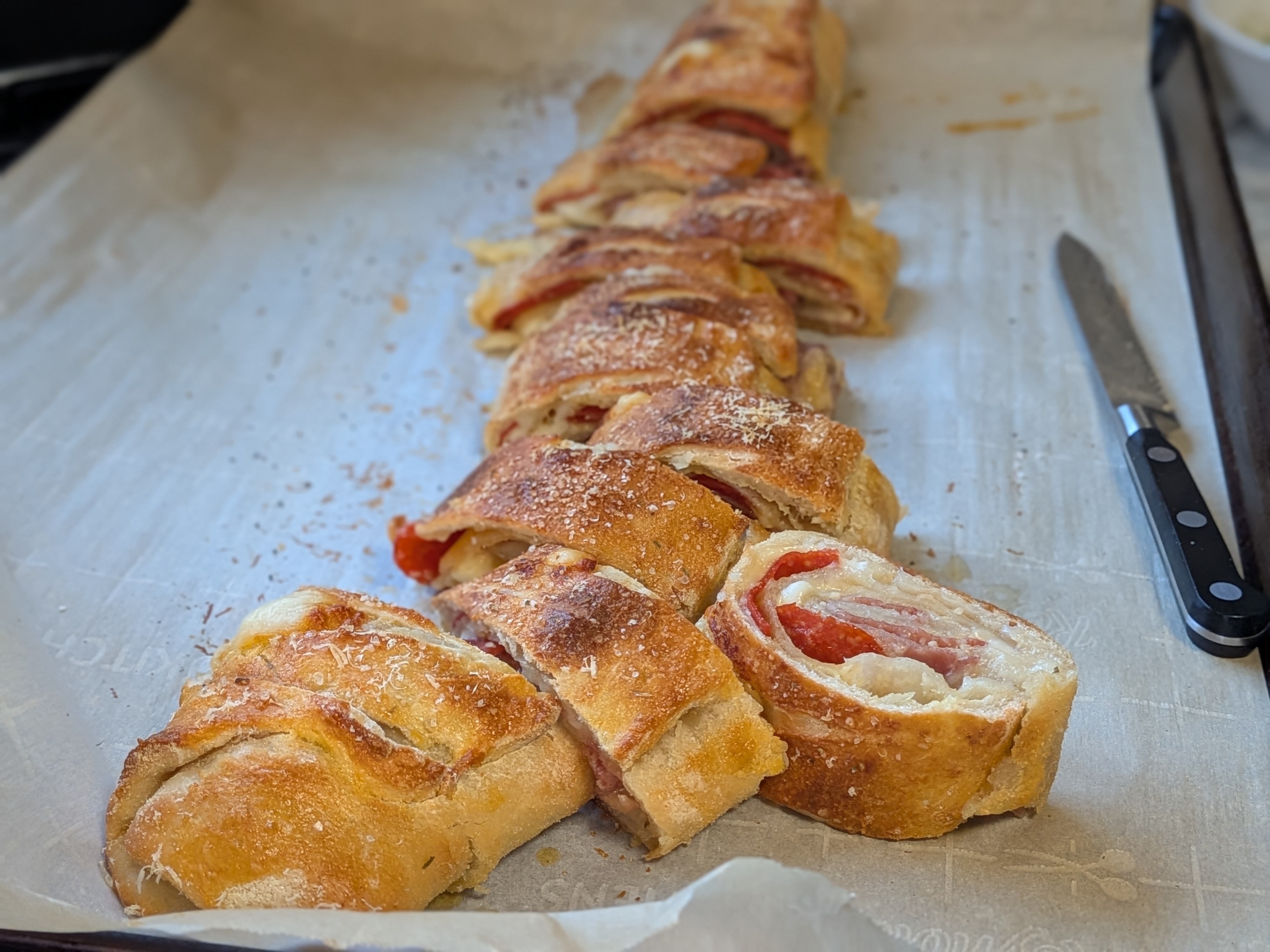 Sliced Italian meats and cheese stromboli on parchment paper showing the scored top crust and the spiral filling of salami, pepperoni, prosciutto, and melted mozzarella and provolone in the cut rounds
