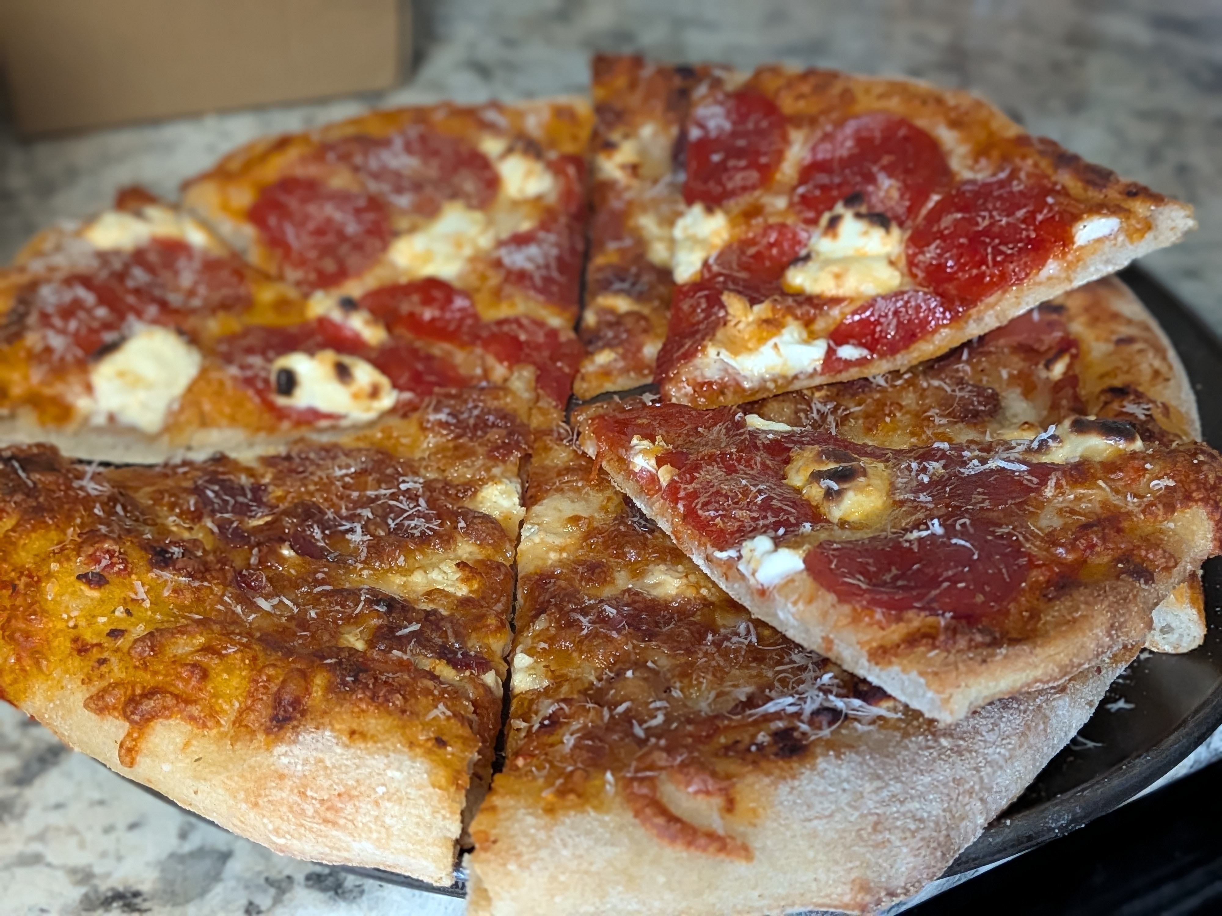 Bacon and feta pizza in front and pepperoni and cream cheese pizza behind, both fresh out of the oven and sliced into wedges