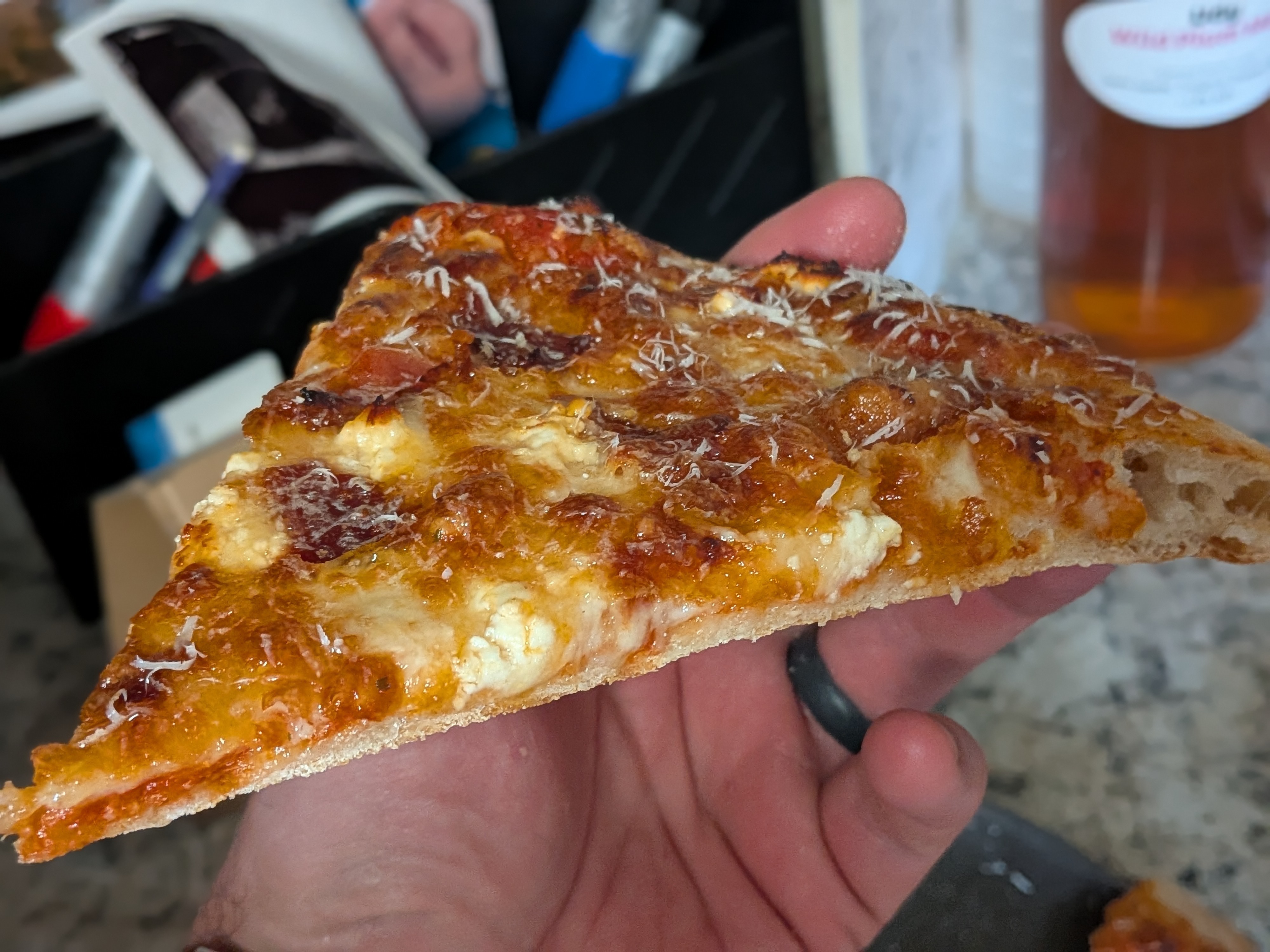 Bacon and feta pizza slice held in hand showing the crisp crust profile and the open crumb at the back