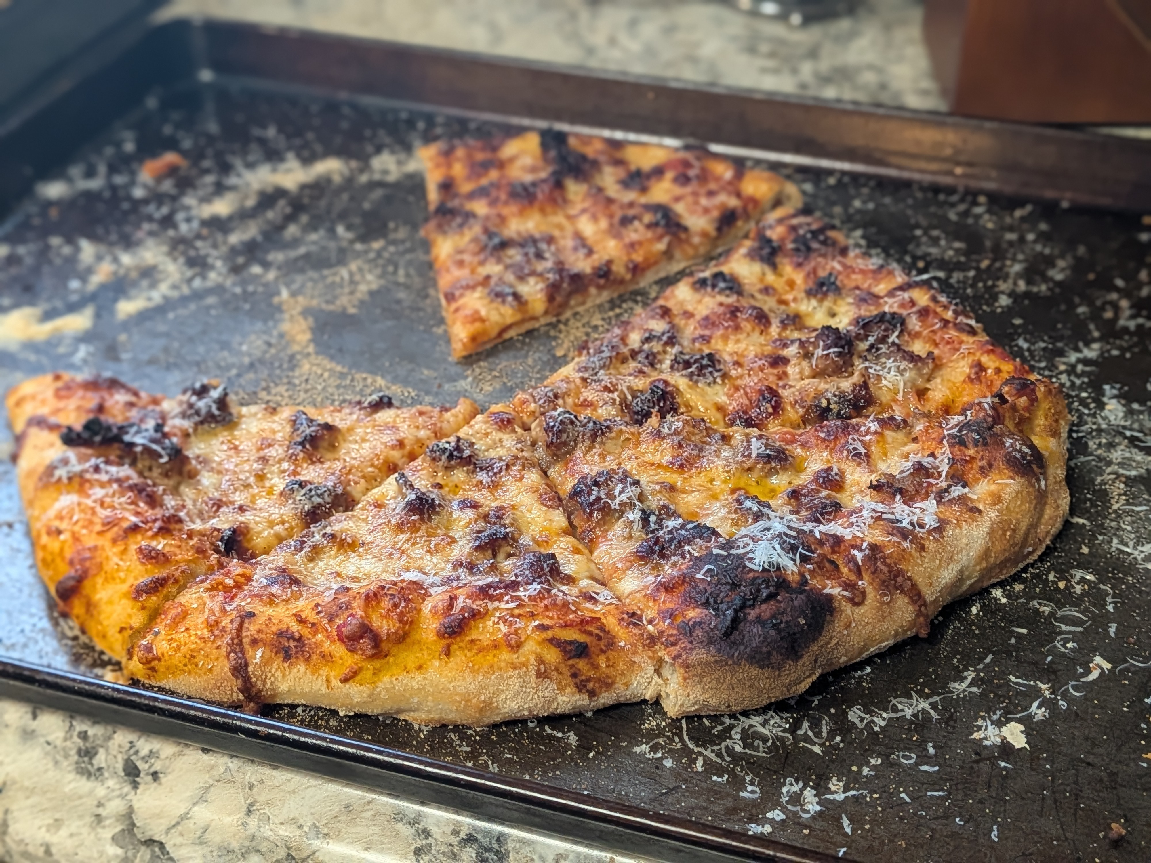 Italian sausage pizza fresh out of the oven on a dark pizza pan, charred top and sliced into wedges