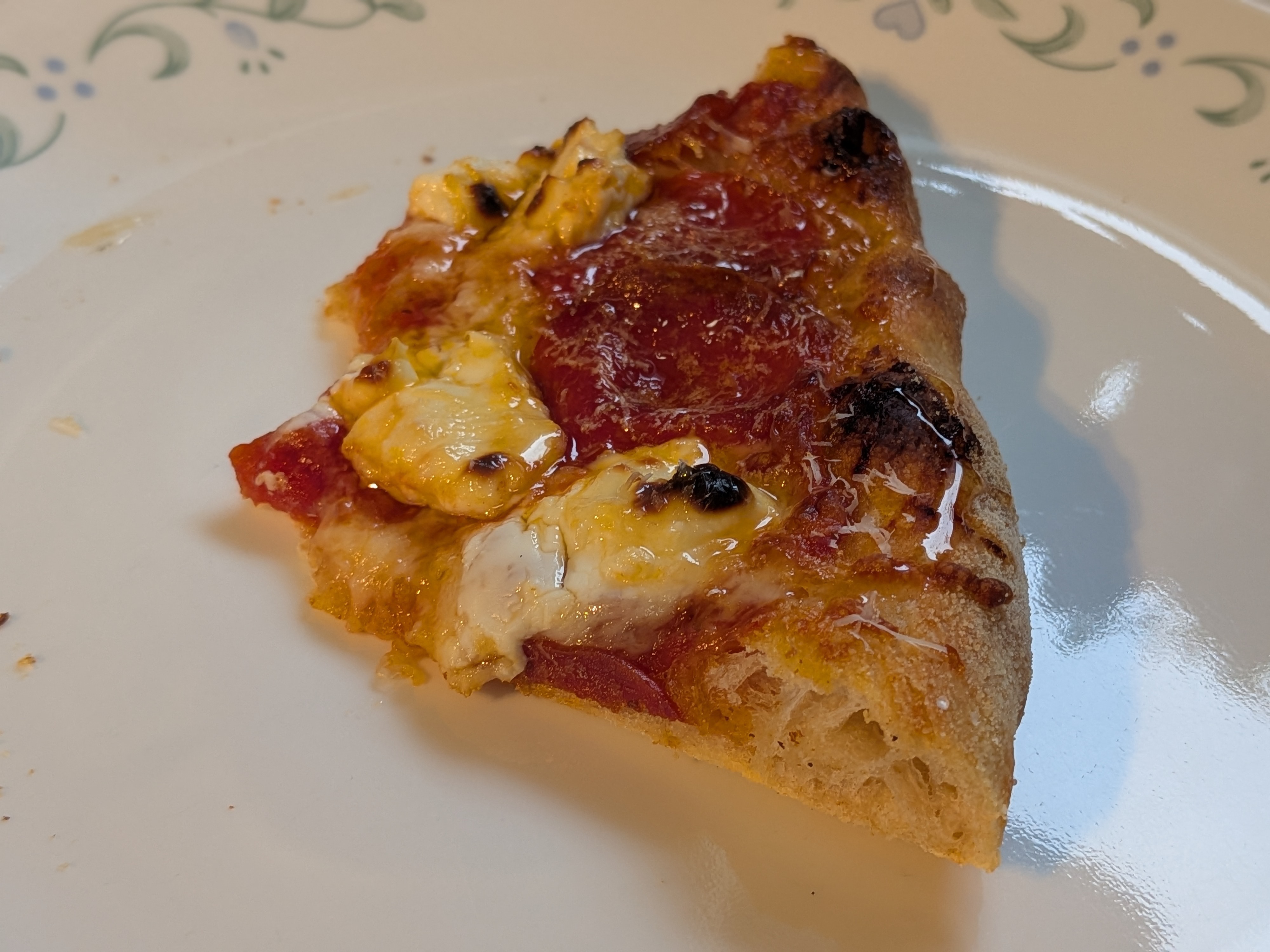Pepperoni and cream cheese pizza slice with hot honey drizzle on a patterned dinner plate