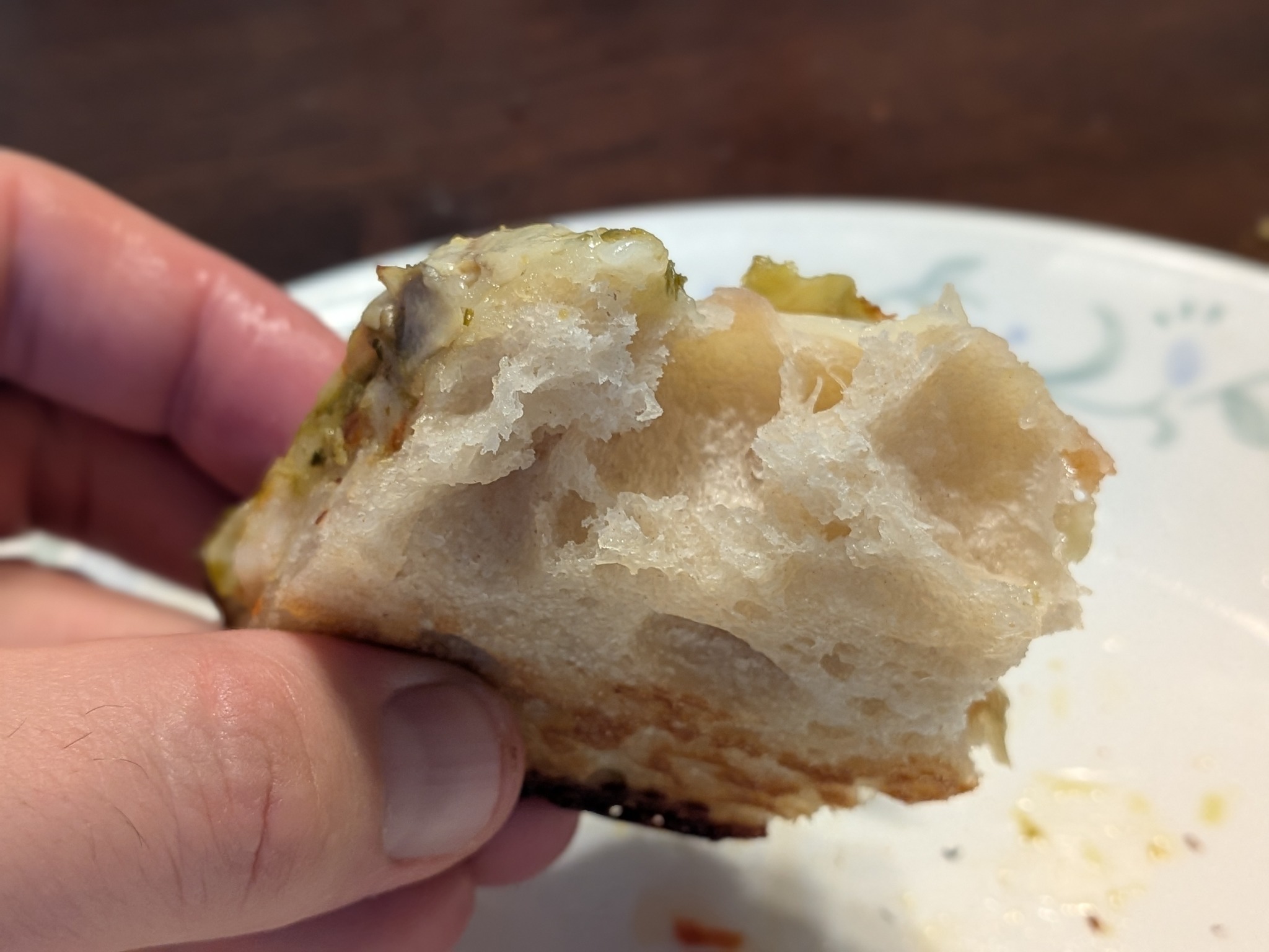 Shrimp and pesto Detroit pizza slice held in hand, showing the open airy crumb structure inside the slice with large irregular holes and well-developed gluten